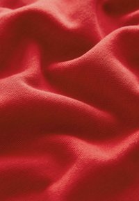 Tissu en coton rouge avec une texture lisse, présentant des plis doux et fluides ainsi qu'un léger stretch sur la surface.