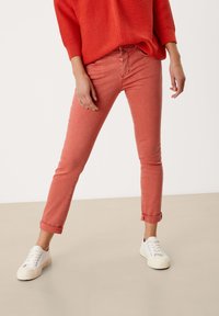 Koraalkleurige jeans met een slim fit, opgerolde manchetten en een klassiek vijf-pocketdesign, gecombineerd met witte veterschoenen.