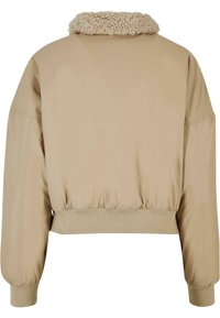 Giacca beige corta con colletto peloso, polsini elastici e orlo. Presenta un esterno liscio e dettagli cuciti.