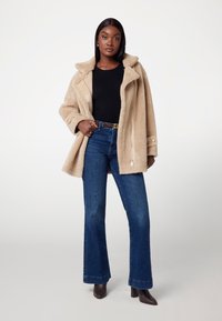 Bež jakna iz umetnega krzna z širokim ovratnikom, v kombinaciji s črno majico in razširjenimi modrimi jeans hlačami. Rjavi čevlji s peto dopolnjujejo videz.