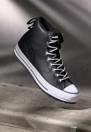 Black high-top sneaker made of textured leather, featuring white laces, a white rubber toe cap, and a treaded black outsole.