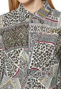 Leopardenmusterhemd mit gemischten Mustern in Schwarz, Weiß und Gold, mit einem Kragen und Knopfverschlüssen. Strukturierter Stoff.