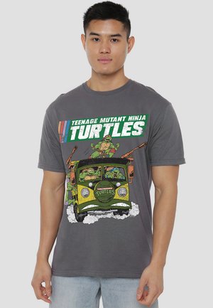 Man wearing grey Teenage Mutant Ninja Turtles shirt featuring turtles driving and standing on a vintage van with action lines and smoke.