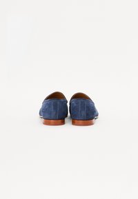 Pantofi din piele albastră cu toc jos și vârf rotunjit. Designul include coasere vizibile și o branț din piele maro. Textură simplă, netedă.