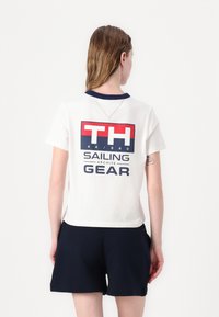 Bomulds T-shirt i off-white med en marinefarvet krave, prydet med et stort grafisk print i rød og blå, og korte ærmer.