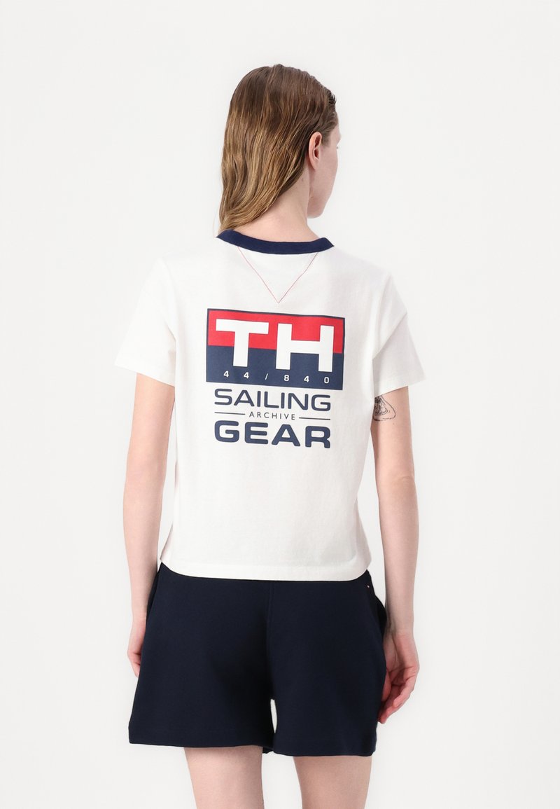 Bomulds T-shirt i off-white med en marinefarvet krave, prydet med et stort grafisk print i rød og blå, og korte ærmer.