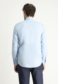 Jasnoniebieska koszula z długim rękawem, zaostrzonym kołnierzykiem, gładką fakturą, mankietami na guziki oraz zaokrąglonym dołem. Brak widocznych wzorów ani akcentów.