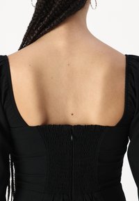 Vestido negro con un escote cuadrado, detalles fruncidos en la cintura y tejido texturizado. Diseño elegante con una silueta ajustada.
