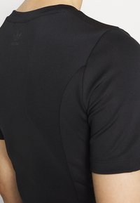 Černé sportovní tričko s krátkým rukávem, vyrobené z hladkého, elastického materiálu. Na zadní straně poblíž výstřihu se nachází decentní logo.