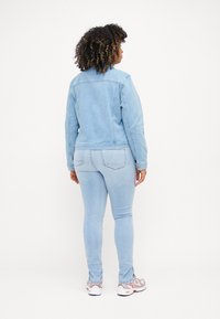 Light blue denim jacket with a standard collar, long sleeves, and buttoned cuffs, paired with matching light blue skinny jeans and multi-colored sneakers.