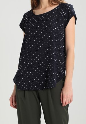 Blusa blu navy a maniche corte, con scollatura rotonda e pois bianchi. Tessuto leggero con una vestibilità leggermente ampia e orlo curvo.