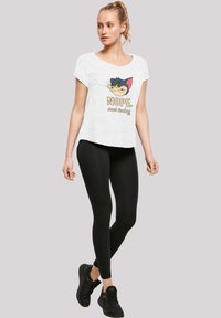 Hvit kortermet t-skjorte med et grafisk katteansikt og tekst som sier "NEI. ikke i dag," kombinert med svarte leggings og svarte treningssko.