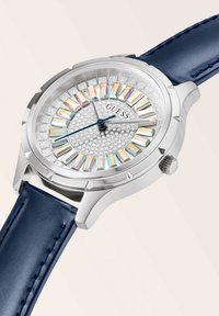Runde silberne Uhr mit einem blauen Lederarmband, ausgestattet mit einem kristallbesetzten Zifferblatt und farbenfrohen rechteckigen Stundenmarkierungen.