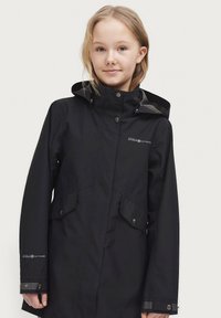 Zwarte waterdichte jas met capuchon, voorzien van twee zakken aan de voorkant, drukknoopsluitingen en een geborduurd logo op de borst en mouw. Zachte textuur.