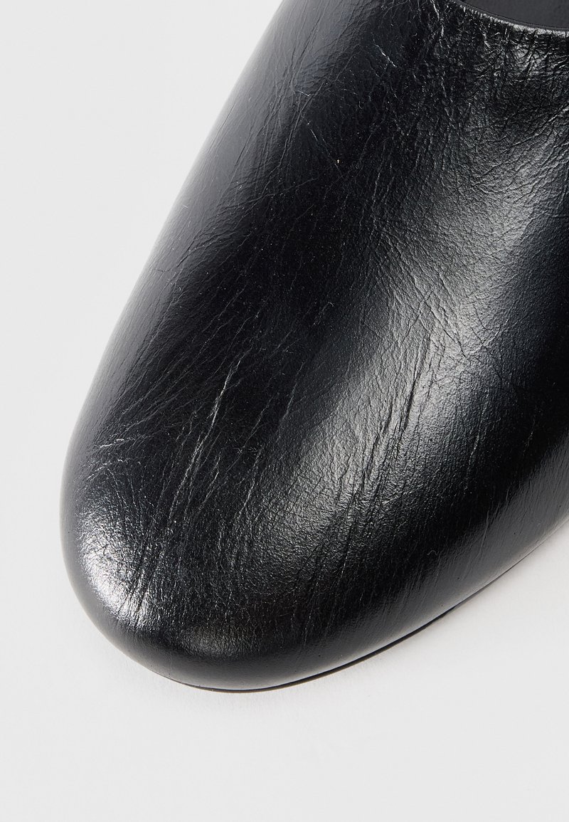 Black leather shoe with a smooth texture, pointed toe design, and subtle creases on the surface, highlighting its craftsmanship.