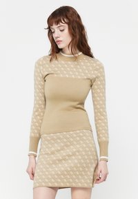 Maglione beige a maglia con motivo geometrico, maniche lunghe, design aderente; abbinato a una gonna coordinata con motivo simile e dettagli a trim.