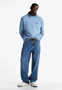 Jasnoniebieska bluza z denimu, z logo. Połączona z jasnoniebieskimi spodniami typu wide-leg i białymi sneakersami.