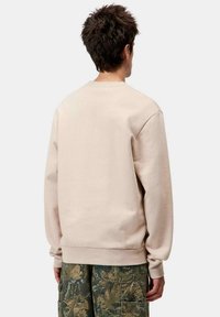 Sudadera de cuello redondo beige en tejido suave, con mangas largas y puños de canalé, combinada con pantalones cargo de camuflaje. Sin logotipos ni patrones visibles.