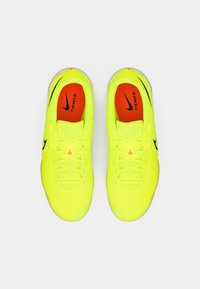 Scarpe da sport Nike Tiempo di un brillante giallo con loghi swoosh neri e soletti rossi, viste dall'alto su uno sfondo bianco.
