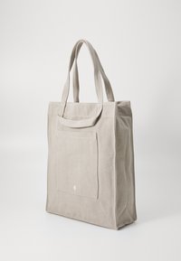 Gray canvas tote bag with two fabric handles, front pocket, and white logo detail. Simple, structured shape with textured finish.
