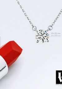 Collier en argent avec un pendentif rond en diamant clair (6,50 mm). À côté, un tube de rouge à lèvres hexagonal rouge avec des accents en argent.