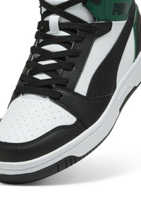 Czarno-białe sportowe buty z chropowatej skórki, perforowanym noskiem, czarnymi sznurowadłami i zielonymi akcentami na pięcie.