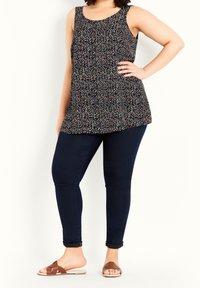 Schwarzes ärmelloses Oberteil mit buntem Blumenmuster, kombiniert mit dunkelblauen Skinny-Jeans und braunen Riemchensandalen. Glatter Stoff und lockere Passform.