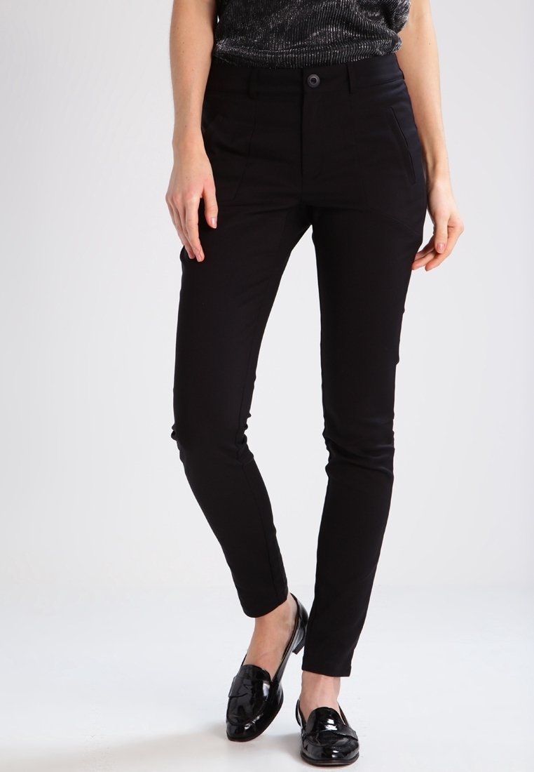 Pantalons noirs ajustés avec une texture lisse, poches latérales et fermeture par bouton. Associés à des mocassins noirs brillants.