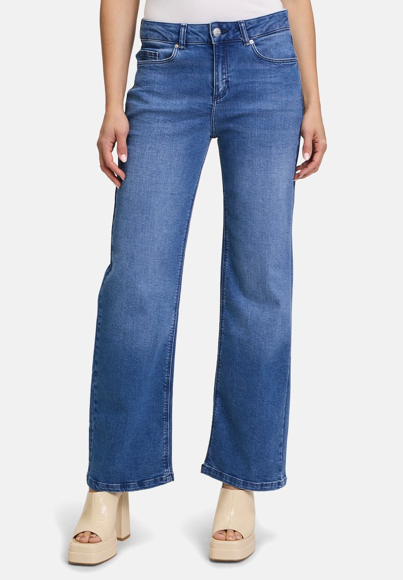 Blaue weit geschnittene Jeans aus Denim, mit hoher Taille, frontalen Taschen und Gürtelschlaufen. Getragen mit hellen Plateausandalen.