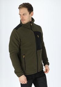 Giacca in pile verde oliva con una tasca sul petto con zip nera. Presenta un colletto alto, tessuto testurizzato e pannelli neri a contrasto sulle spalle.
