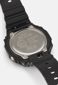 Black Casio GA-2100GB watch with a stainless steel back, digital display, and textured rubber strap featuring multiple holes for adjustments.