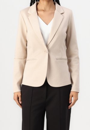 Beige skræddersyet blazer med enkelt knaplukning, klappede reverser og frontlommer. Glat stof, parret med mørke bukser.