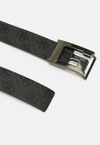 Ceinture noire à motifs en matériau texturé, dotée d'une boucle métallique avec un nom de marque en relief, des bords lisses et un design épuré.