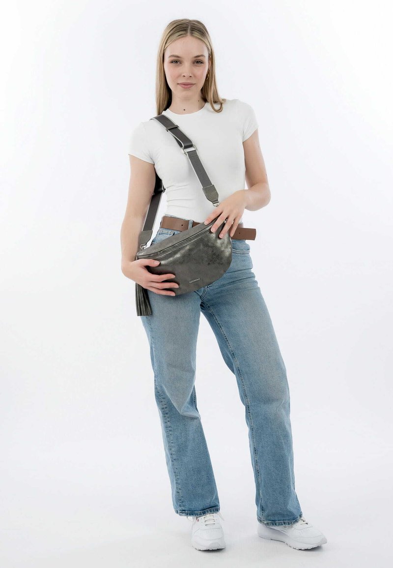 Borsa a tracolla in pelle grigia con chiusura a zip e dettaglio con frange, abbinata a jeans blu chiaro e una camicia bianca aderente.