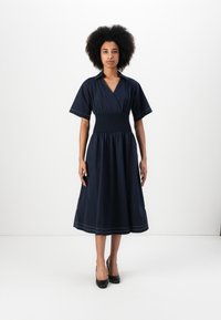 Vestido azul marinho com cintura franzida ajustada, mangas curtas e decote em V; possui um detalhe de ponto à máquina discreto na barra.