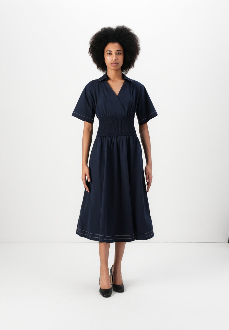 Vestido azul marinho com cintura franzida ajustada, mangas curtas e decote em V; possui um detalhe de ponto à máquina discreto na barra.