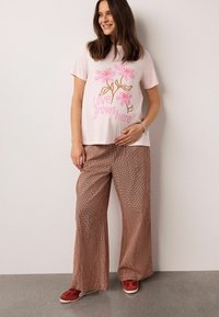 Rožinės spalvos medvilniniai marškinėliai su gėlių atspaudu ir užrašu „Čia auga meilė“. Derinami su rudos spalvos languotomis plačiomis kelnėmis ir raudonais sportbačiais.