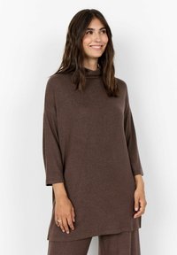 Tunic marrone, oversize, con collo alto, maniche a tre quarti e un tessuto morbido e testurizzato. L'orlo scende sotto i fianchi.