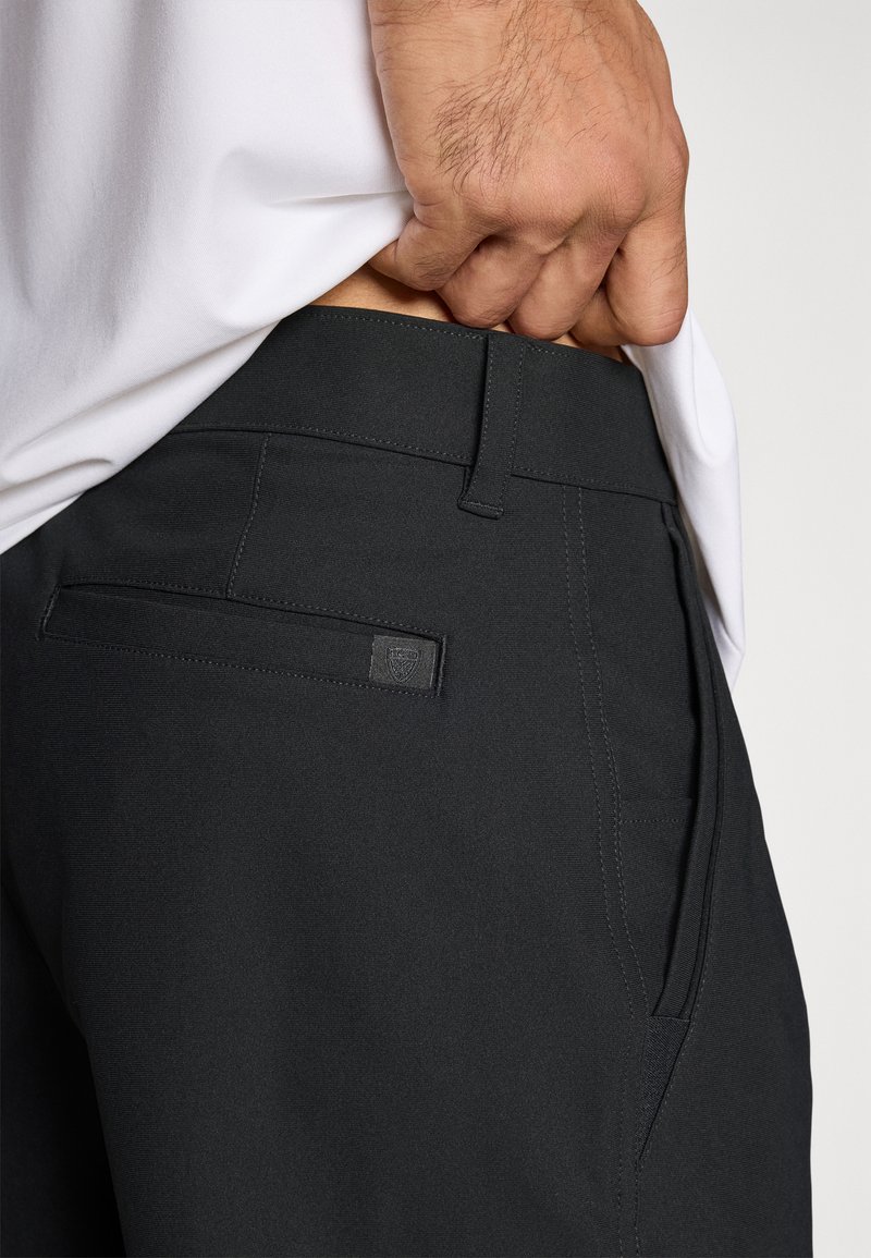 Pantalon noir à texture lisse, doté d'une poche arrière et d'un marquage subtil. La ceinture est plate avec des coutures pour la structure.