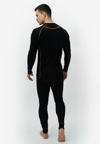 Zwarte thermoshirt en -broek met gele stikselaccenten, smalle pasvorm, lange mouwen en een ronde halslijn. Glad materiaal met een gelaagd ontwerp.