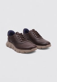 Zapatillas de cuero marrón con un diseño redondeado, acabado texturizado y suela ligera beige. Presentan cierre con cordones y cuello acolchado.