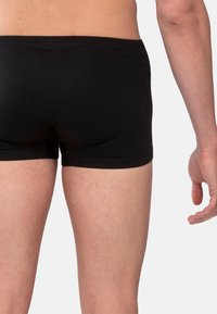 Boxer-briefs en coton noir avec une coupe ajustée, présentant une ceinture lisse et un design minimaliste, visibles sur un fond clair.