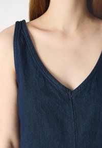 Σκοτεινό μπλε τζιν αμάνικο τοπ με σχέδιο V-λαιμού, με διακριτές ραφές και λεία υφή.