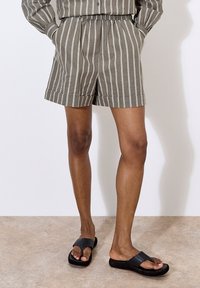 Pantalones cortos a rayas verde oliva con un corte relajado, cinturilla elástica y puños enrollados, combinados con sandalias tipo slide negras.