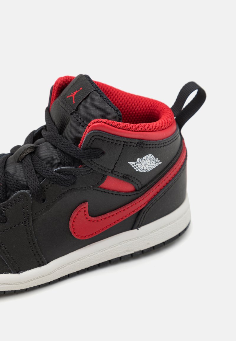 Baskets montantes noires et rouges en cuir et mesh, avec une surface texturée, un Swoosh Nike proéminent et un logo Air Jordan.