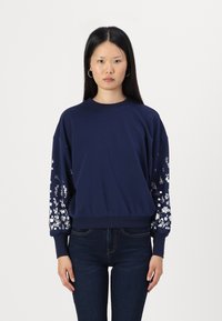 Marinblå sweatshirt med blommönster på puffärmar, ribbade muddar och nederkant. Tillverkad av mjukt material, har en avslappnad passform och rundad halsringning.