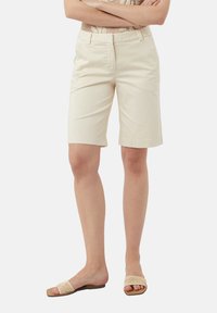 Pantaloni corti beige fino al ginocchio realizzati in tessuto elasticizzato con una texture liscia, caratterizzati da un frontale piatto, tasche laterali e passanti per cintura.