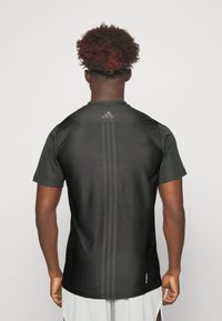 Camiseta deportiva negra de manga corta, con laterales de malla, textura suave, que cuenta con tres rayas verticales y un logo en la parte superior de la espalda.