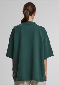 Veľká tmavozelená bavlnená tričko s okrúhlym výstrihom a krátkymi rukávmi. Hladká textúra, bez viditeľných vzorov alebo ozdôb.