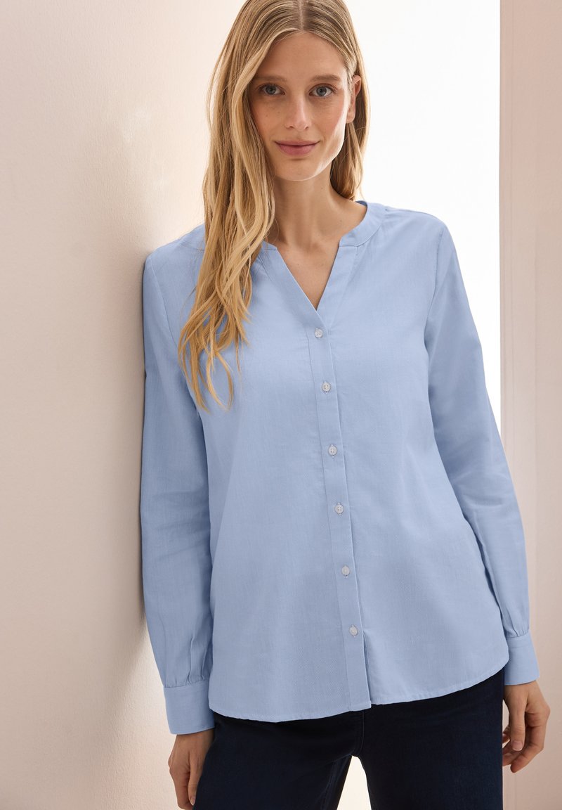Camicia a maniche lunghe di un blu chiaro con scollatura a V e bottoni sul davanti. Realizzata in tessuto morbido, presenta una vestibilità rilassata e una texture sottile.